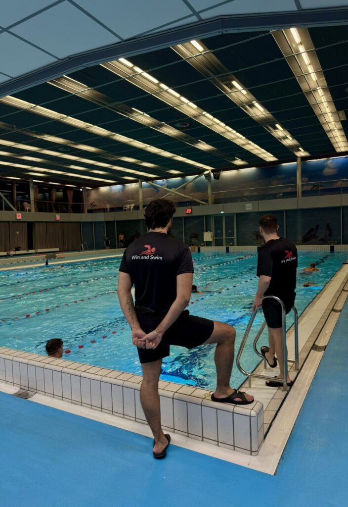 Two coaches watching over the swimming pool with the back at the camera. Observing the swimmers in the water