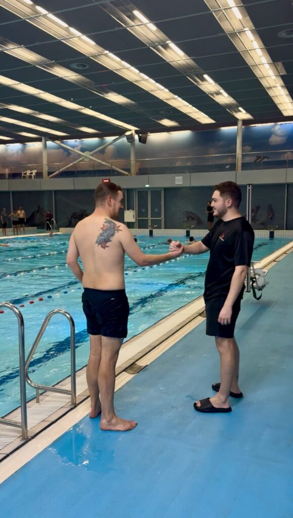 Swimming coach giving personalized feedback to a swimmer at the poolside with the text 'ACHIEVE MORE' overlayed.