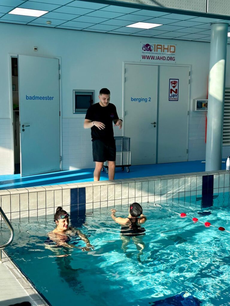 A swimming coach stands by the poolside, instructing two swimmers in the water during a training session